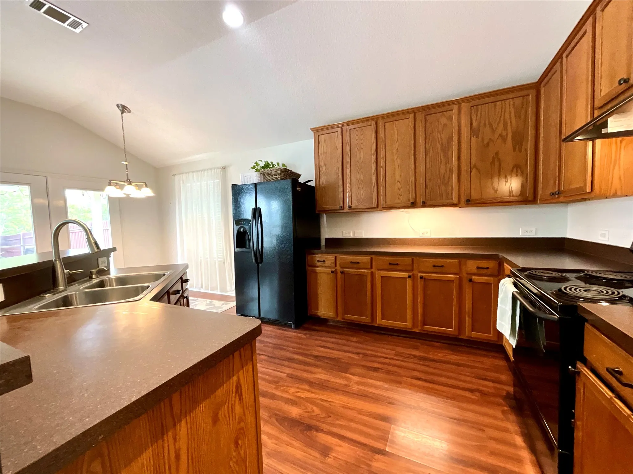 Kitchen featuring wood-finish flooring, wood cabinetry, dark countertops, and a double basin sink with a high-arch faucet