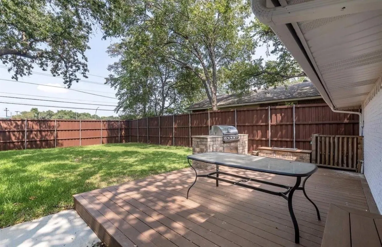 Expansive backyard featuring a wood-finish deck, concrete patio, built-in outdoor grill, and a privacy fence