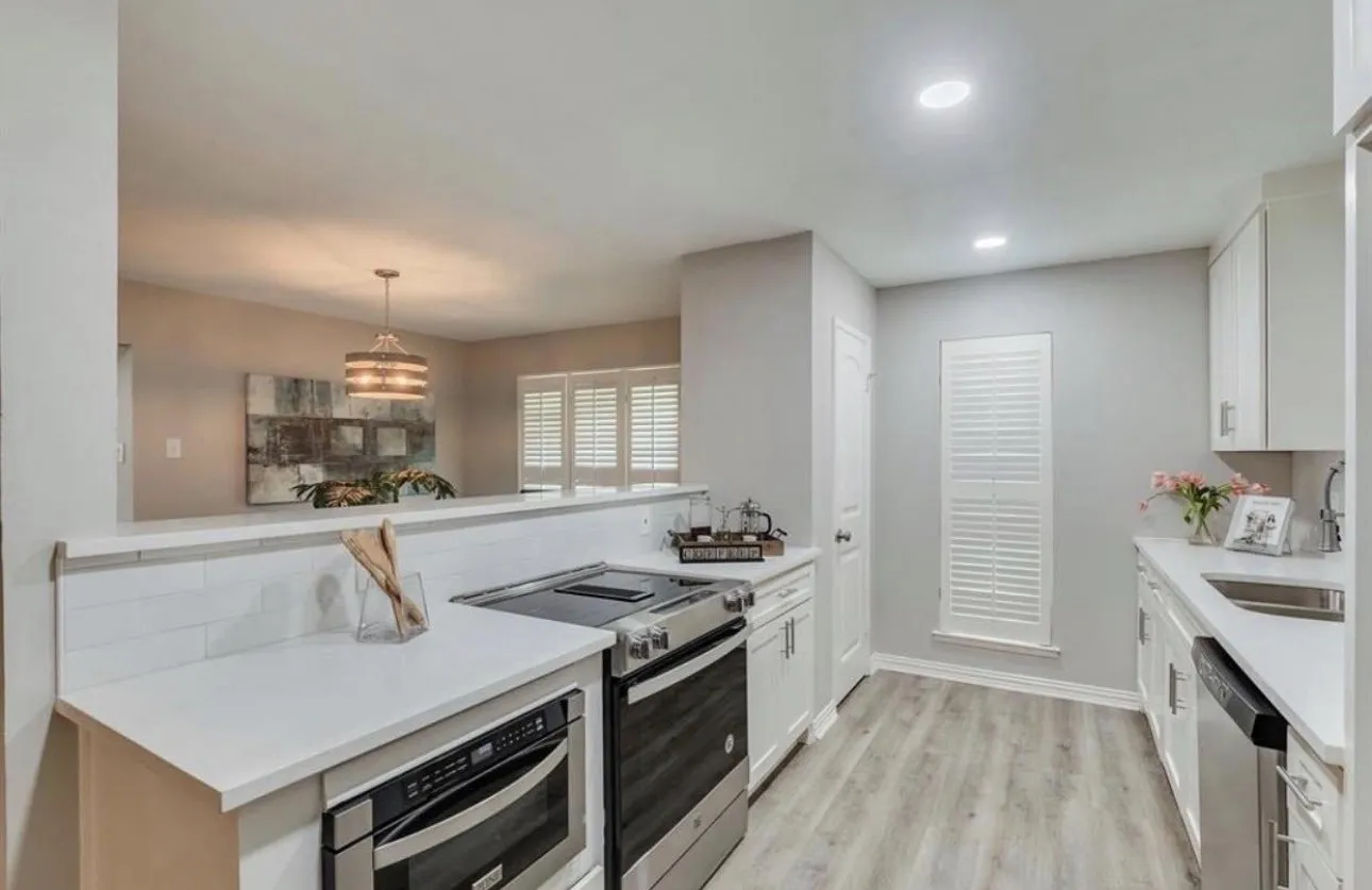 Kitchen with white cabinetry, stainless steel appliances, light countertops, and wood-finish flooring