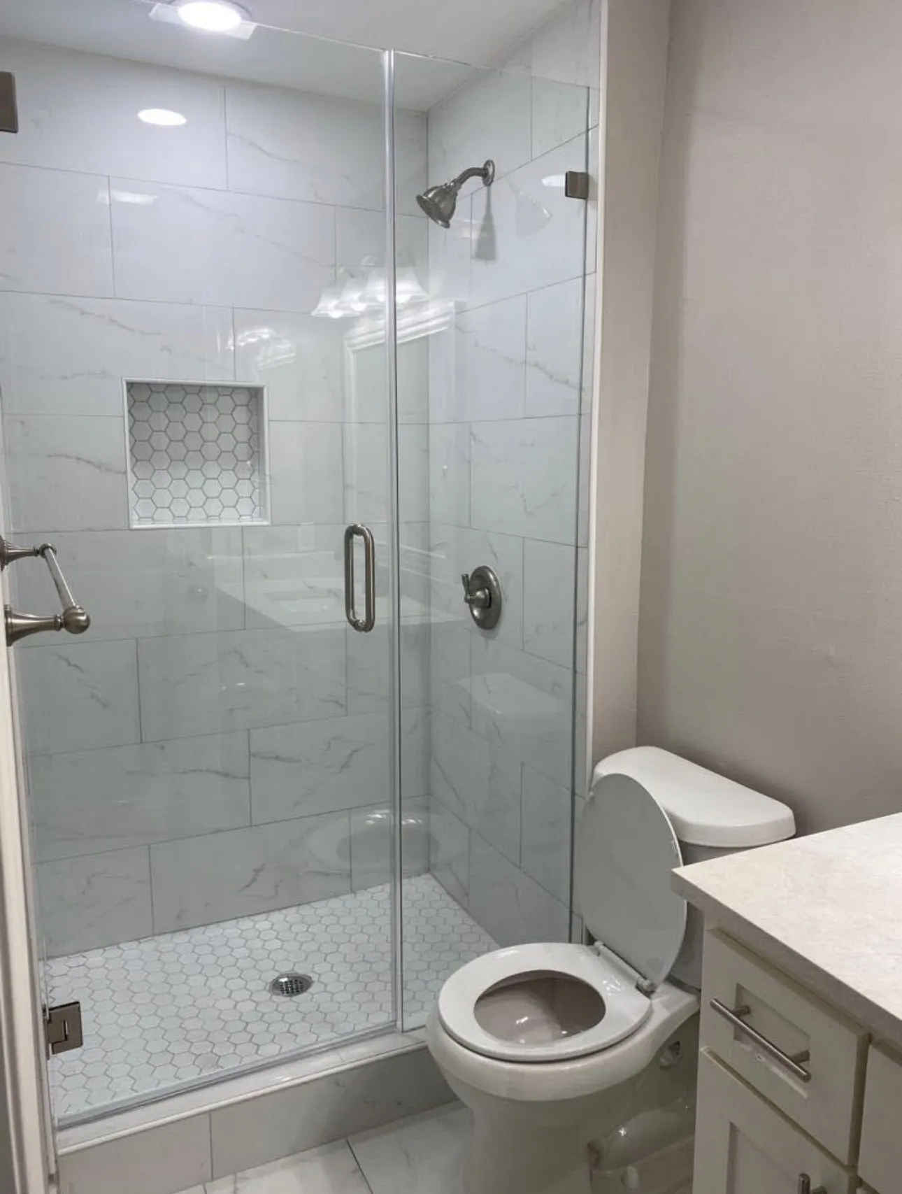 Glass-enclosed shower with white subway tile walls, a hexagonal tile shower floor, and a built-in shower niche