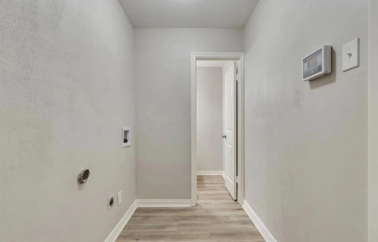 Wood-finish flooring with white trim, light gray painted walls, and a white interior door