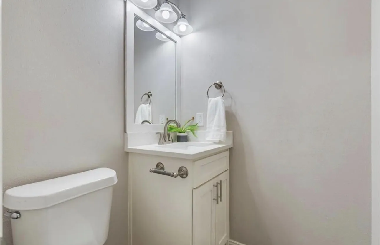 White vanity with integrated sink, chrome faucet, white countertop, and wall-mounted mirror with overhead lighting