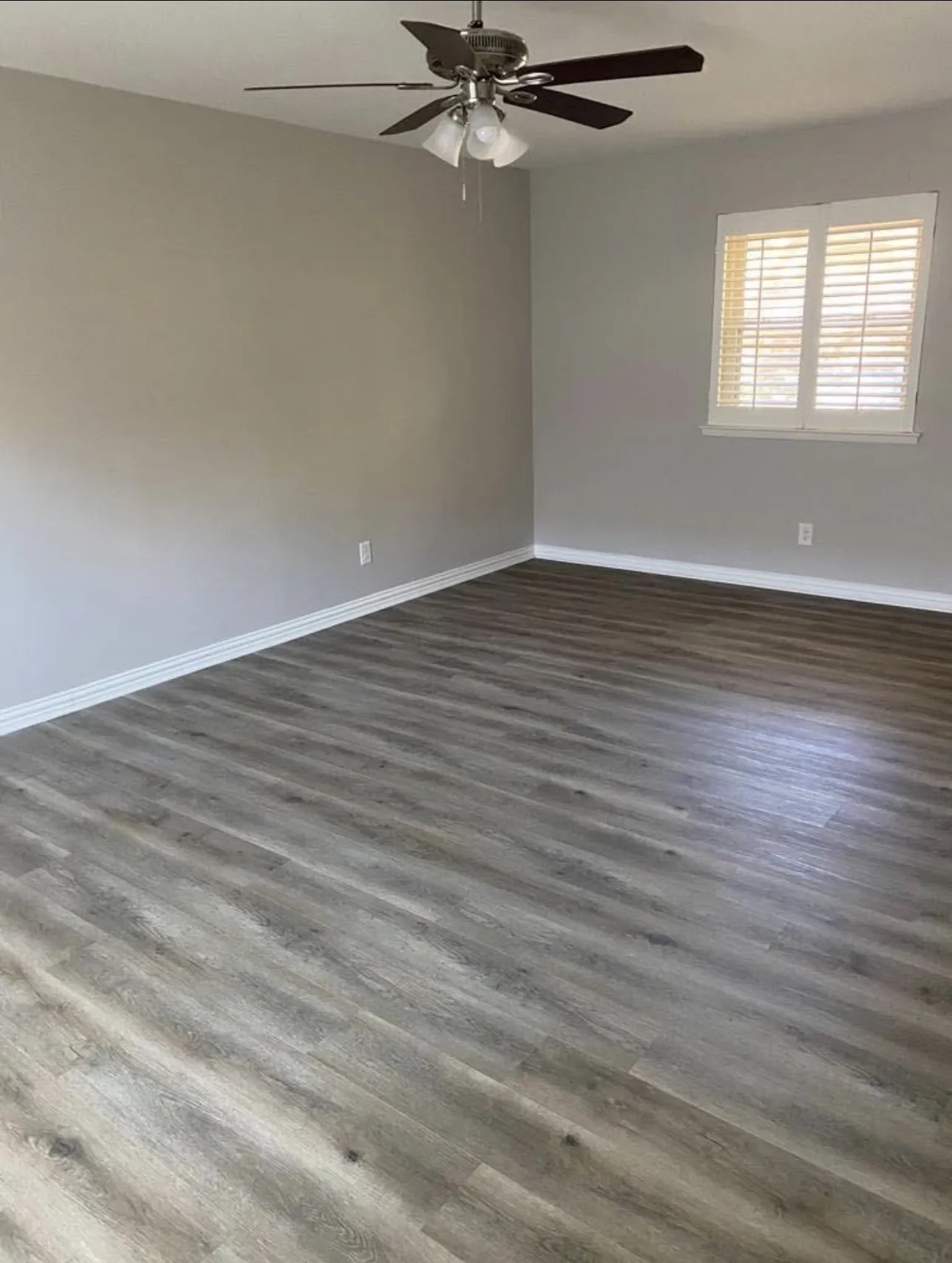 Wood-finish flooring, neutral painted walls, ceiling fan with integrated lighting, and window with plantation shutters