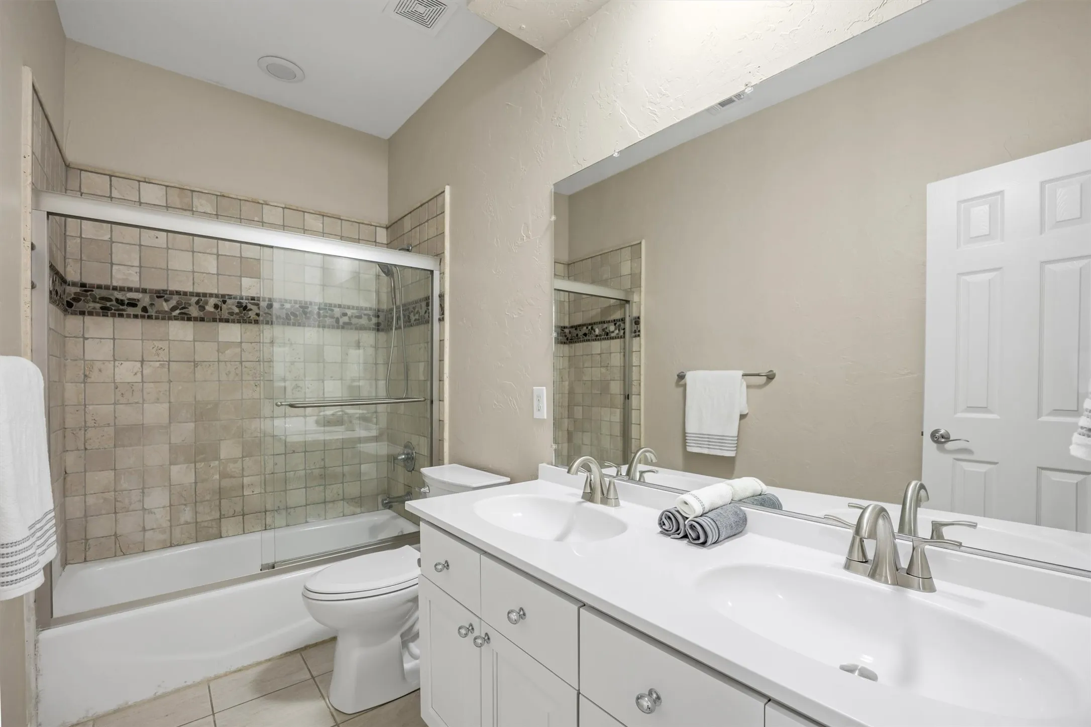 Second bathroom has a Dual vanity with white undermount sinks, brushed nickel faucets, full-width mirror, tub & shower combination, and glass shower doors.