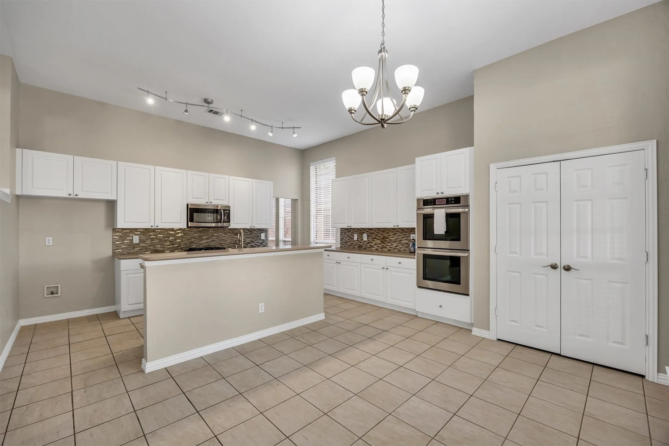 Spacious Kitchen features SS appliances, a mosaic tiled backsplash, a central island, decorative lighting, pantry, and breakfast dining area.