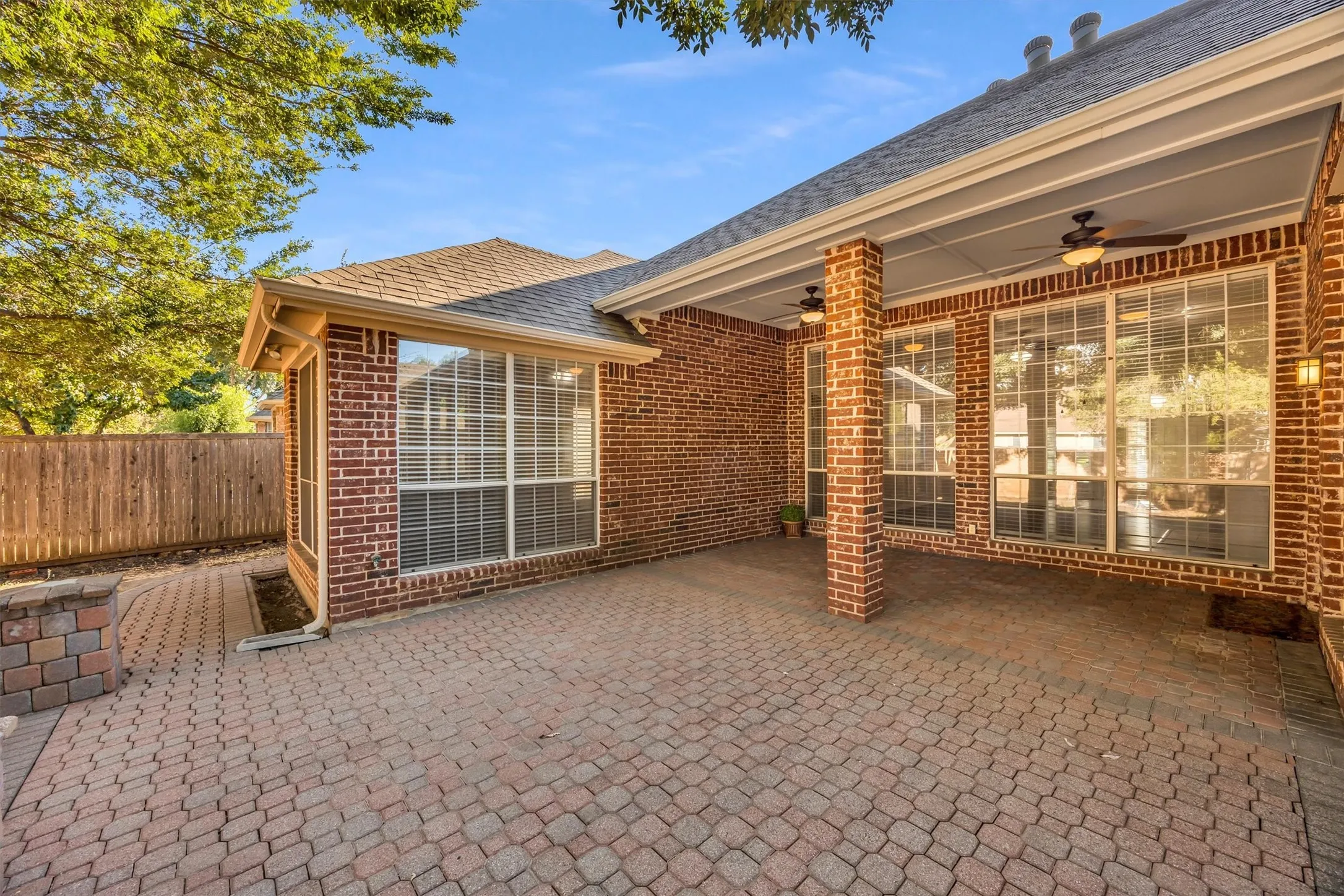 Expansive built-in covered patio, with dual ceiling fans, decorative paver flooring surrounded by large windows from the primary bedroom ensuite, living room, kitchen.