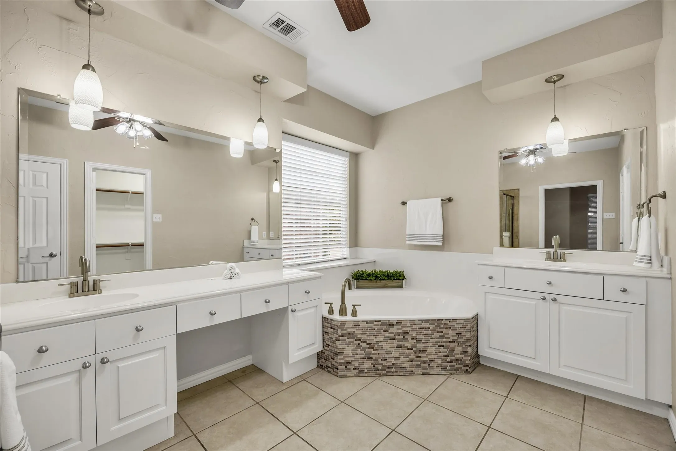 Dual vanities with white cabinets, dressing table area, soaker tub