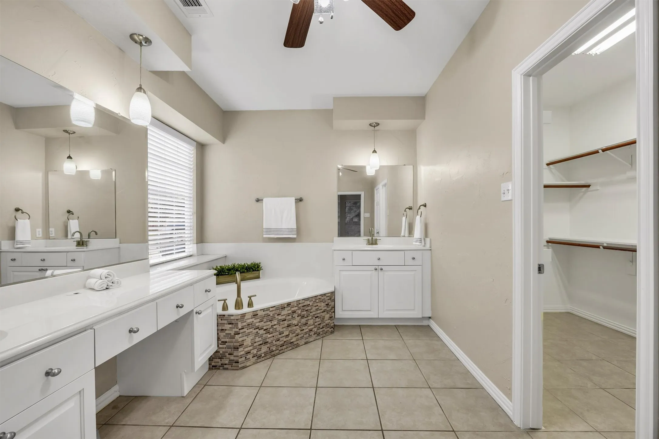 Dual vanity sinks, soaker tub, recessed lighting, and an adjacent walk-in closet with shelving