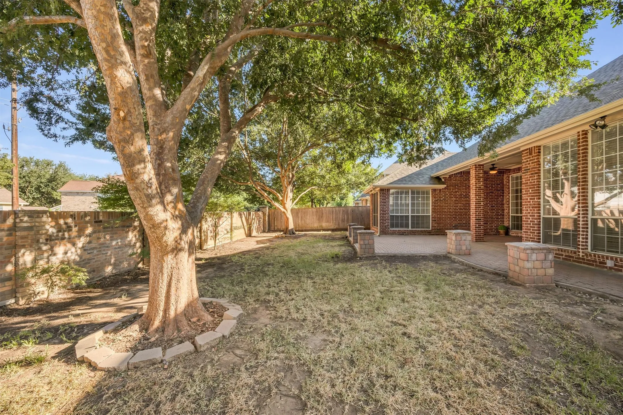 Expansive backyard with a shade trees, brick privacy wall, and wood fencing