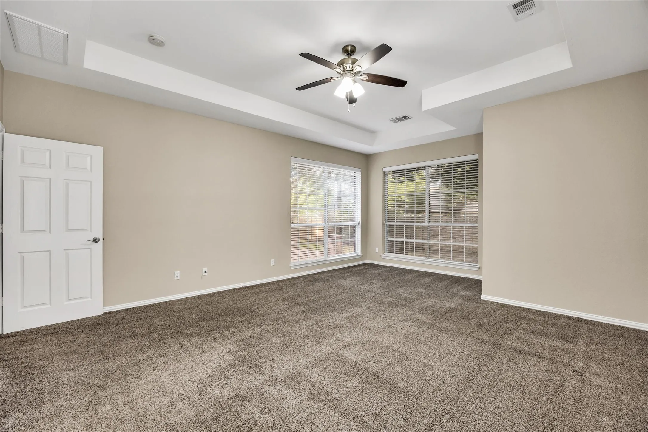 Spacious Primary ensuite bedroom features tray ceilings, carpeting, a ceiling fan, and multiple windows.