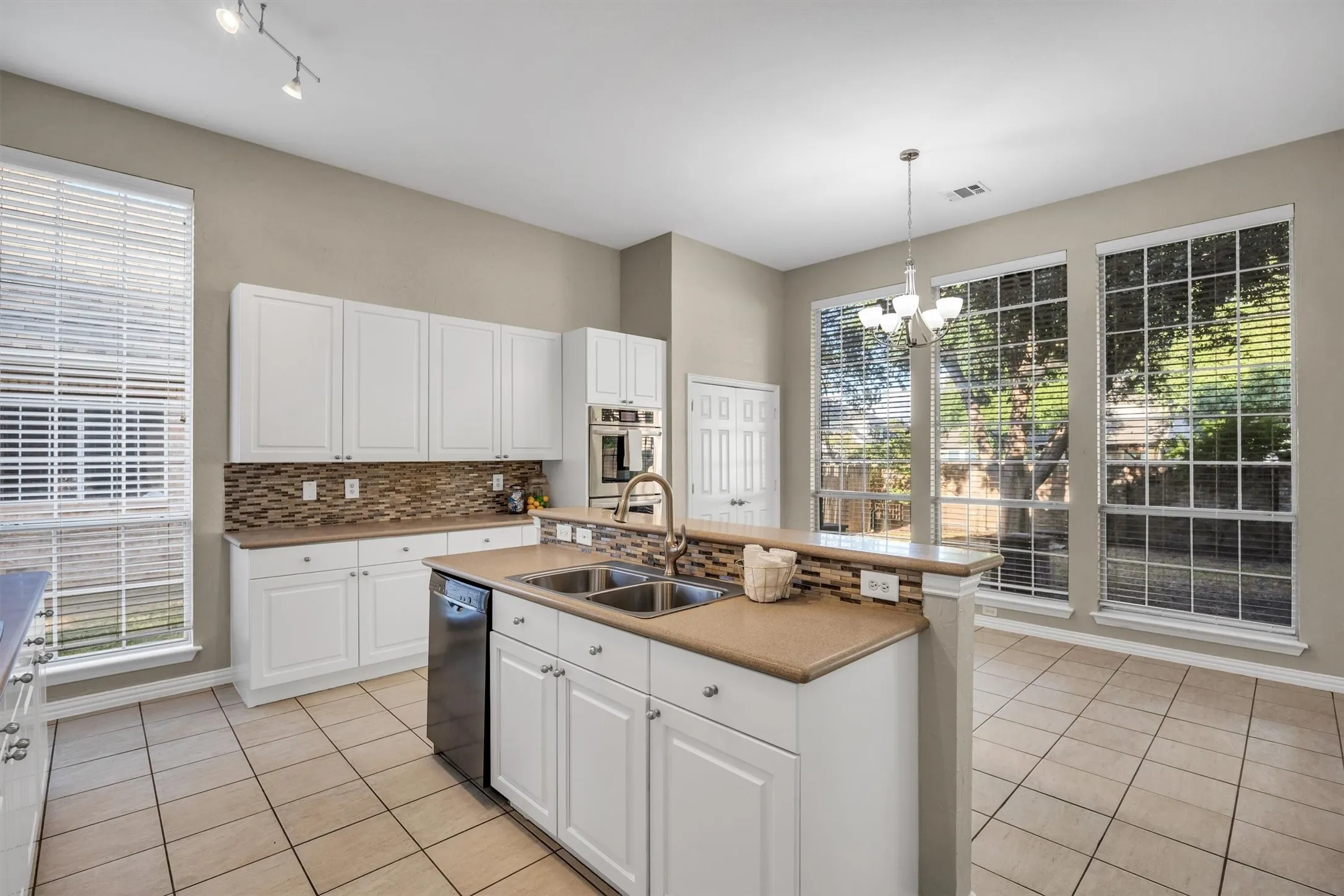 Kitchen features an island with an integrated sink, white cabinetry, Corian® solid counter tops, tile flooring, mosaic tile backsplash, and large windows
for abundant natural lighting.