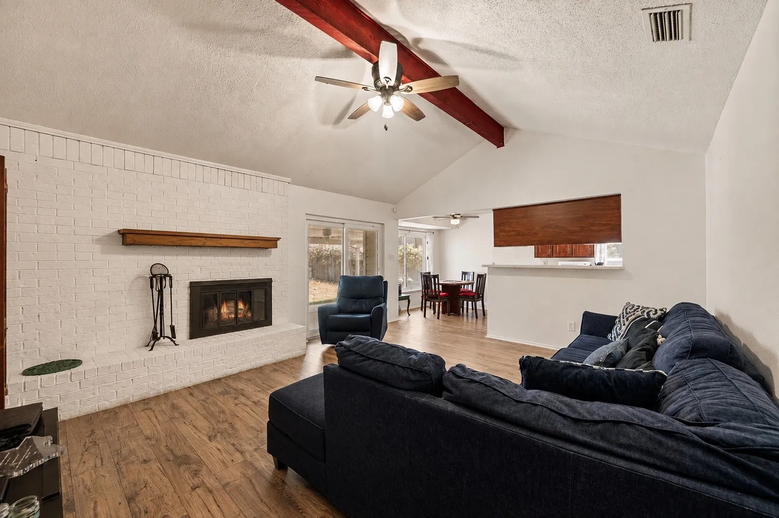 Vaulted ceilings with exposed wood beams, wood-finish flooring, and a white brick fireplace with a wood mantle