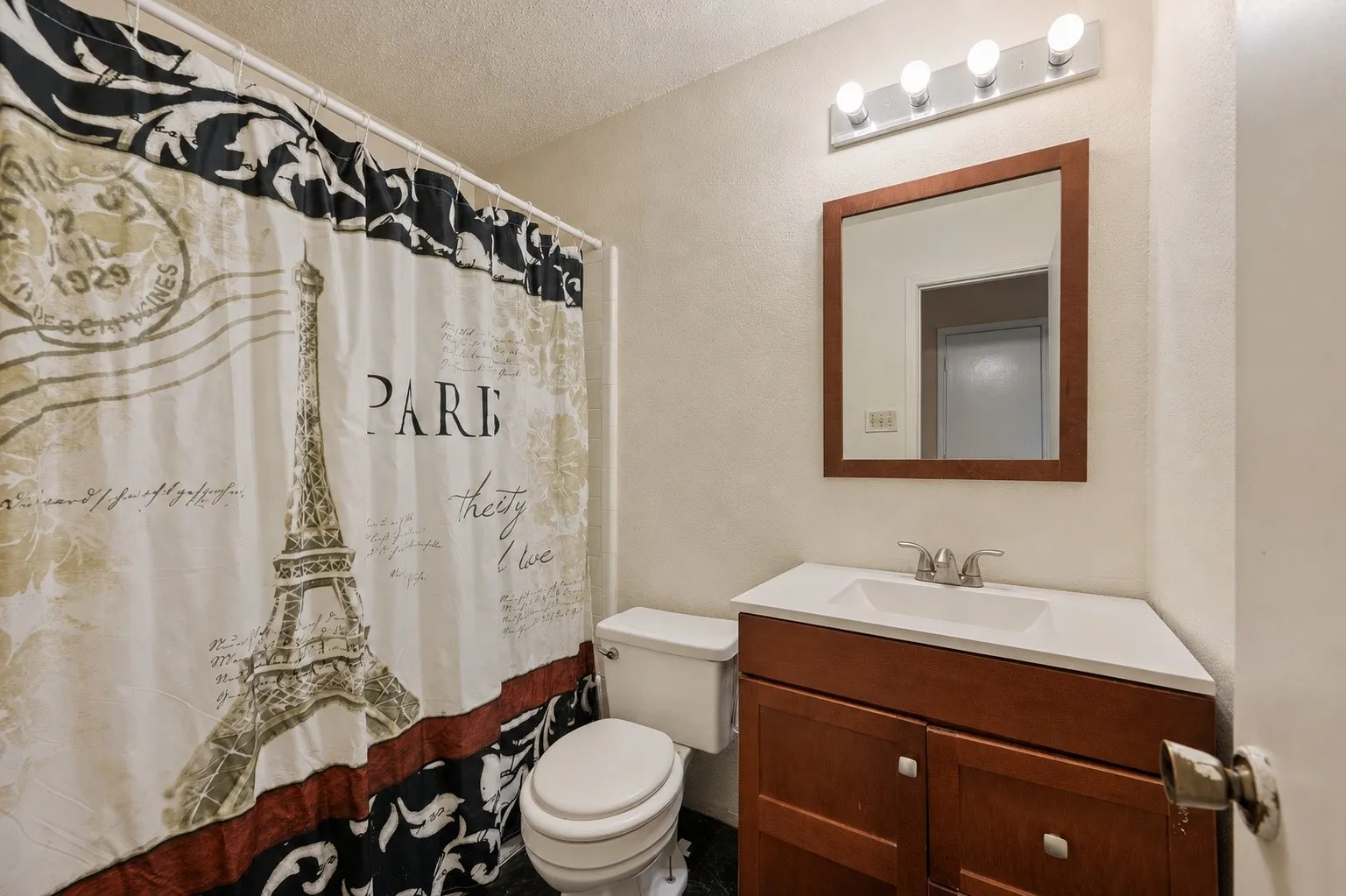 Compact bathroom featuring a wood-finish vanity with an integrated sink, framed mirror, and chrome lighting fixture