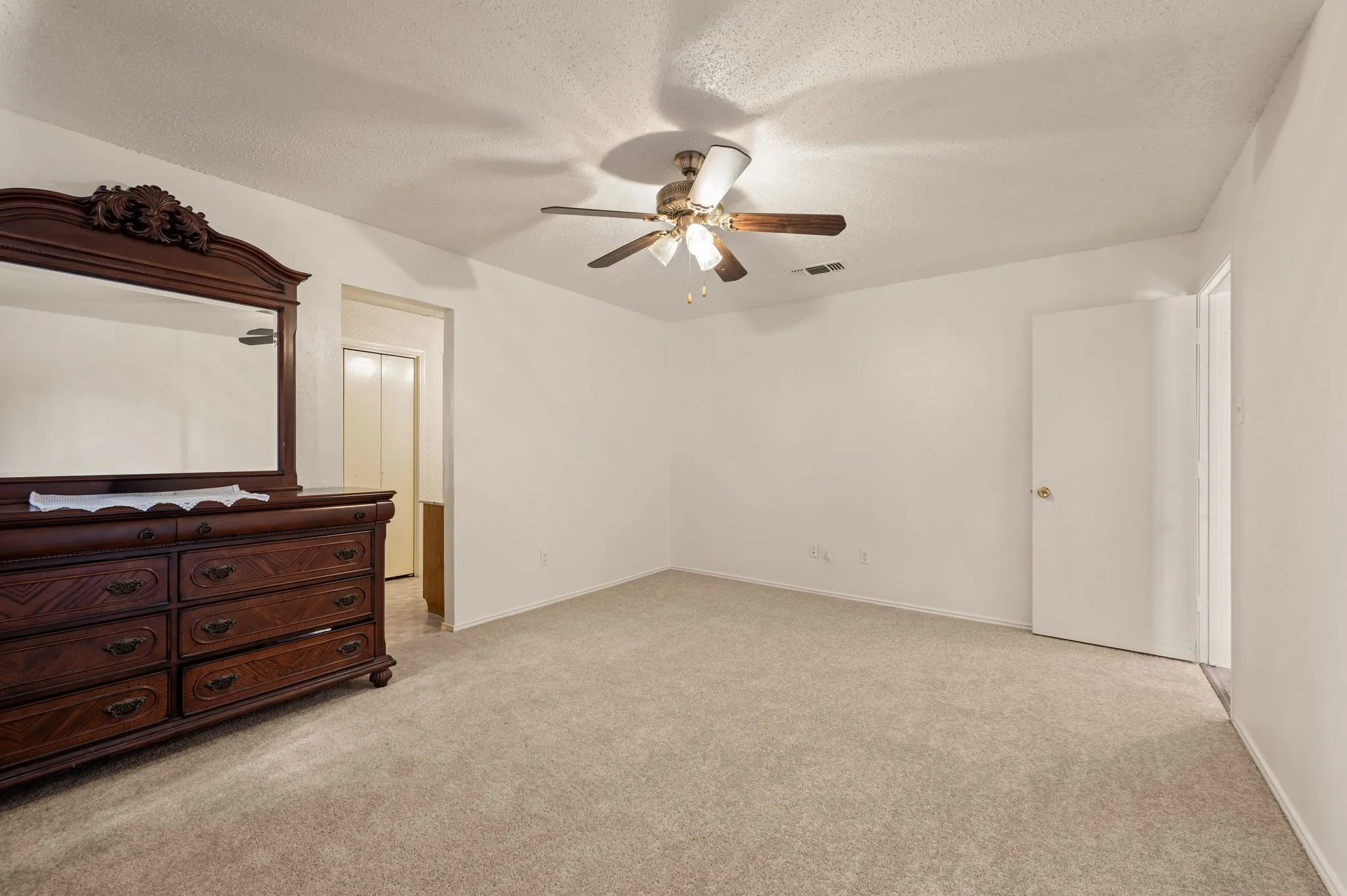 Light-toned carpeting, ceiling fan with integrated lighting, white painted walls, and a white door with brass-tone hardware