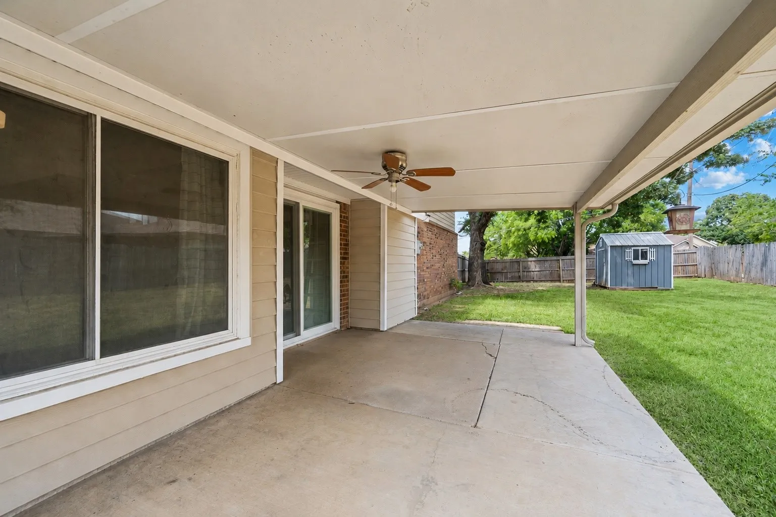 Covered patio with an outdoor ceiling fan, concrete flooring, and sliding glass doors