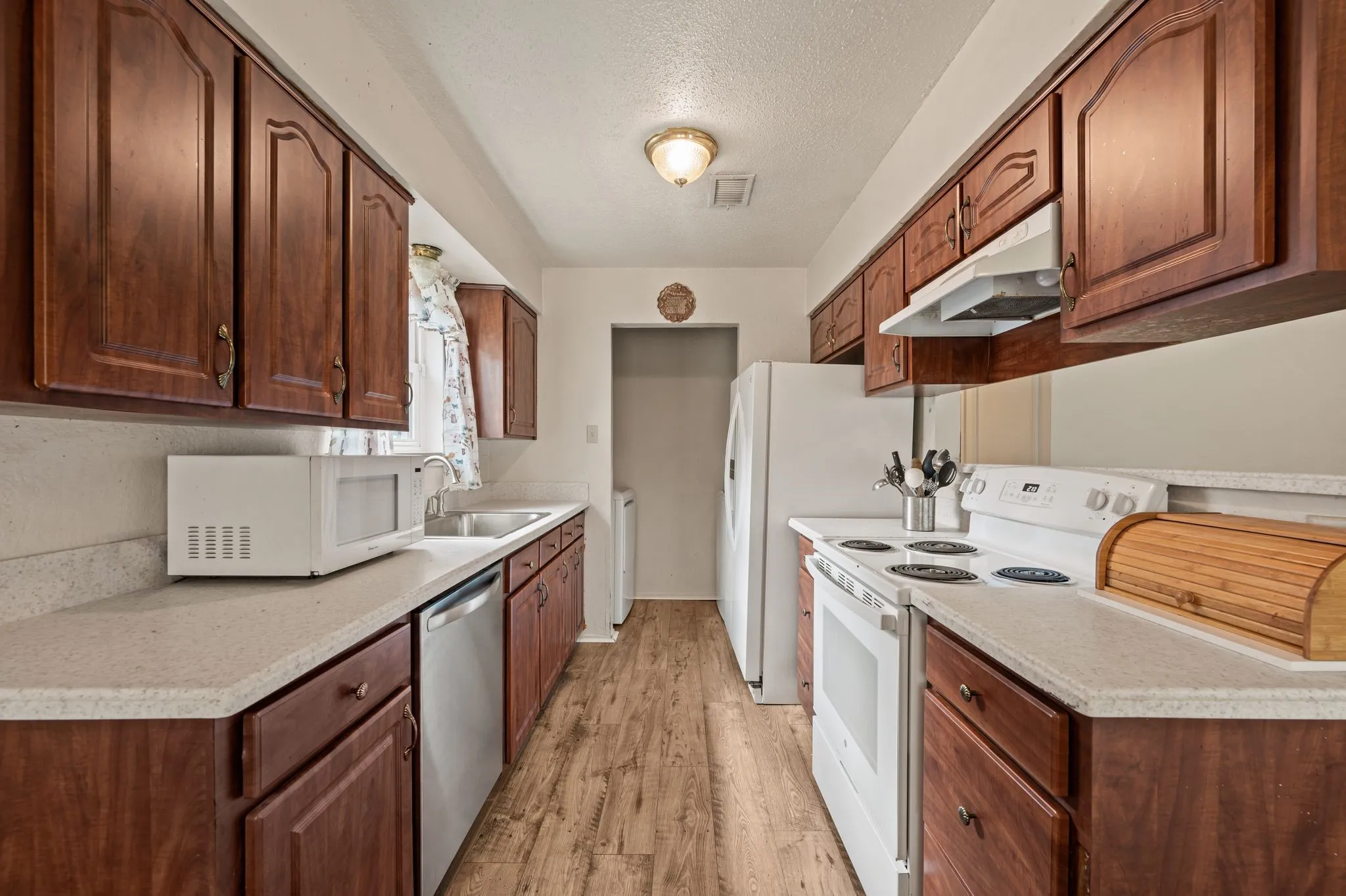 Galley kitchen featuring wood-finish cabinetry, light-toned countertops, and wood-finish flooring
