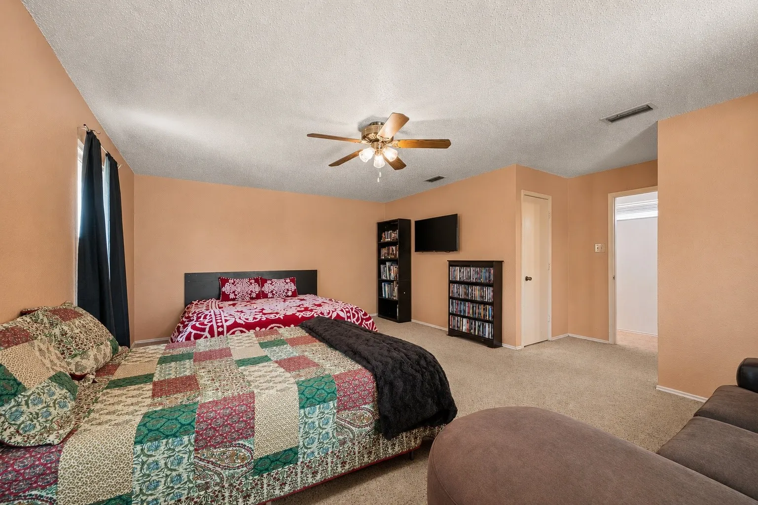 Carpeted interior space with a ceiling fan, wall-mounted television, and a built-in wall niche