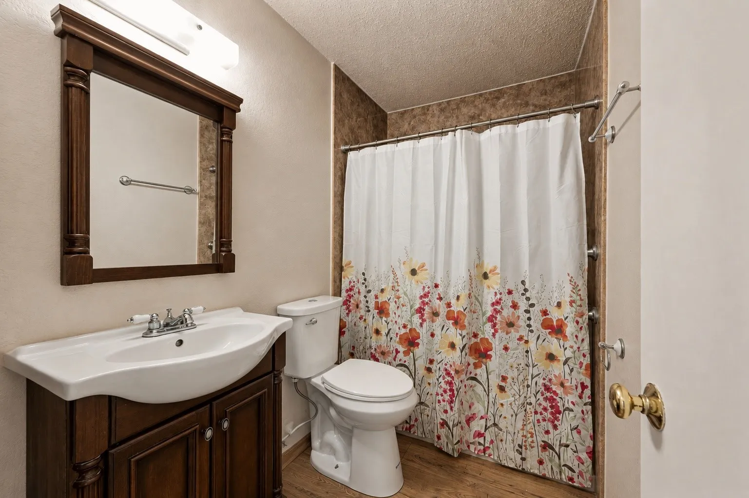 Wood-finish flooring with a vanity featuring a white ceramic sink and a framed mirror