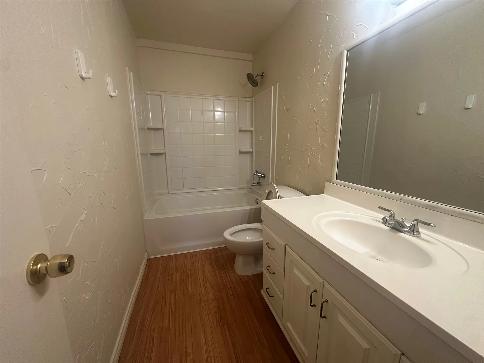Bathroom featuring a white vanity with integrated sink, wood-finish flooring, a full bathtub with a tiled shower surround, and a wall-mounted mirror