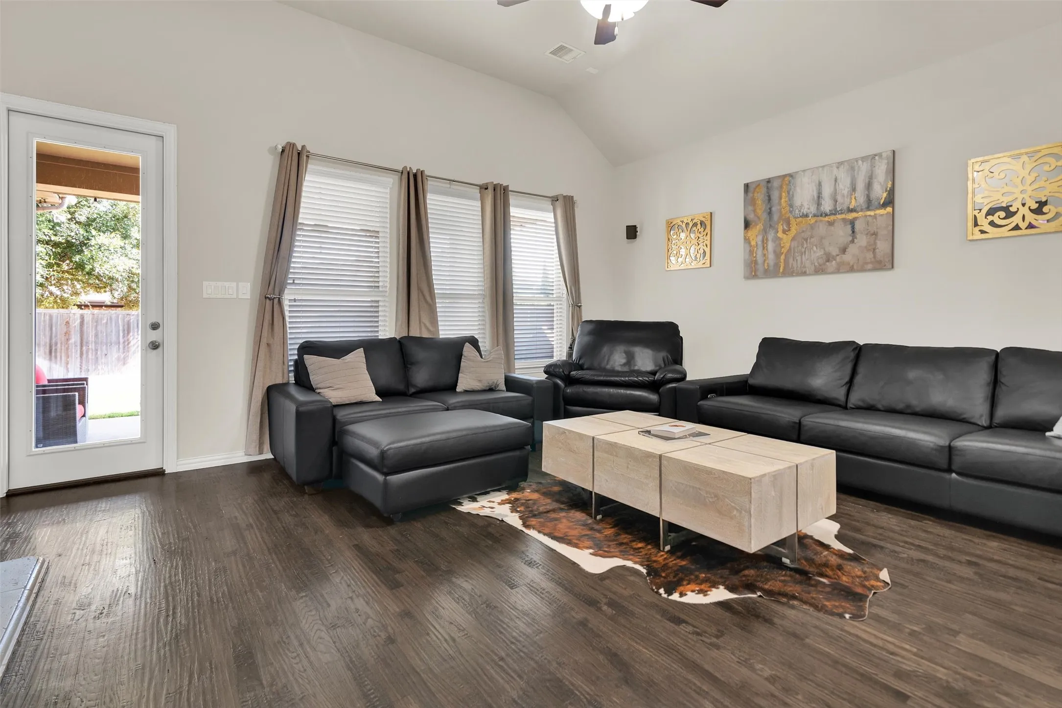 Vaulted ceiling, wood-finish flooring, glass-paneled exterior door, multiple windows, and ceiling fan