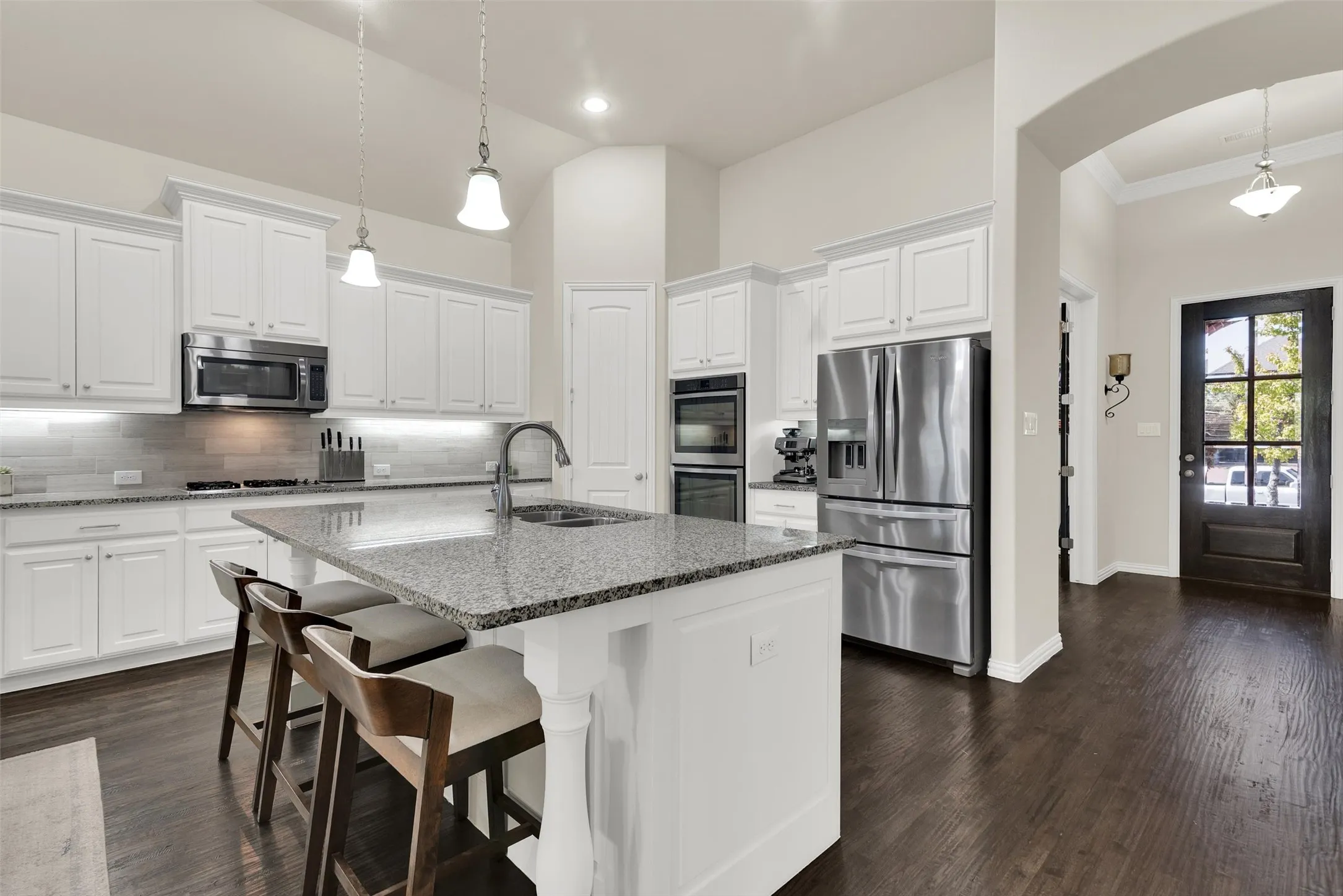 Kitchen featuring white cabinetry, stainless steel appliances, a granite-topped island with an undermount sink, pendant lighting, and dark wood-finish flooring
