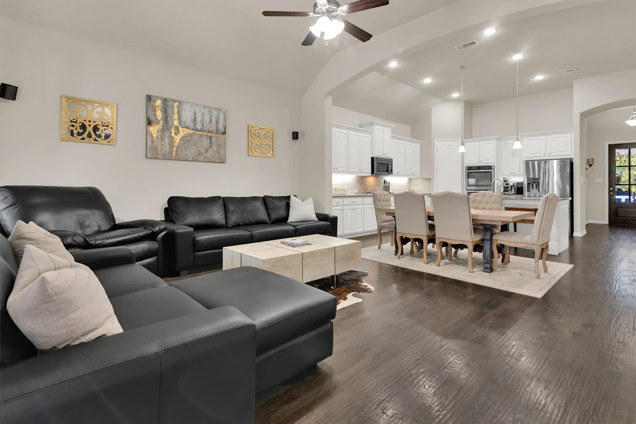 Vaulted ceilings with recessed lighting, wood-finish flooring, white kitchen cabinetry with undermount lighting, stainless steel appliances, and a ceiling fan