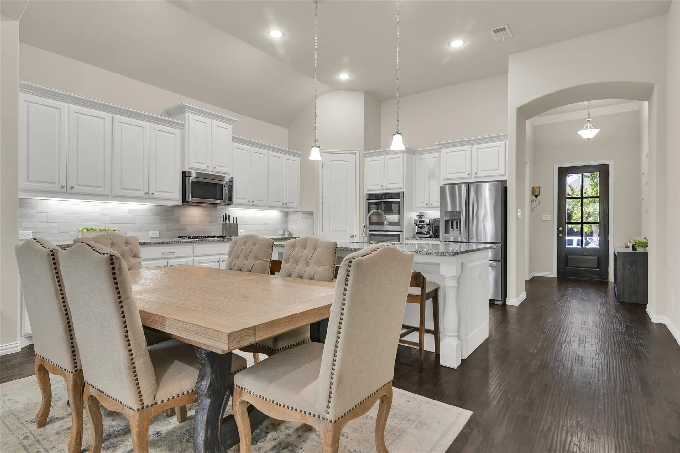 Open-concept kitchen with white cabinetry, stainless steel appliances, granite countertops, and dark wood-finish flooring