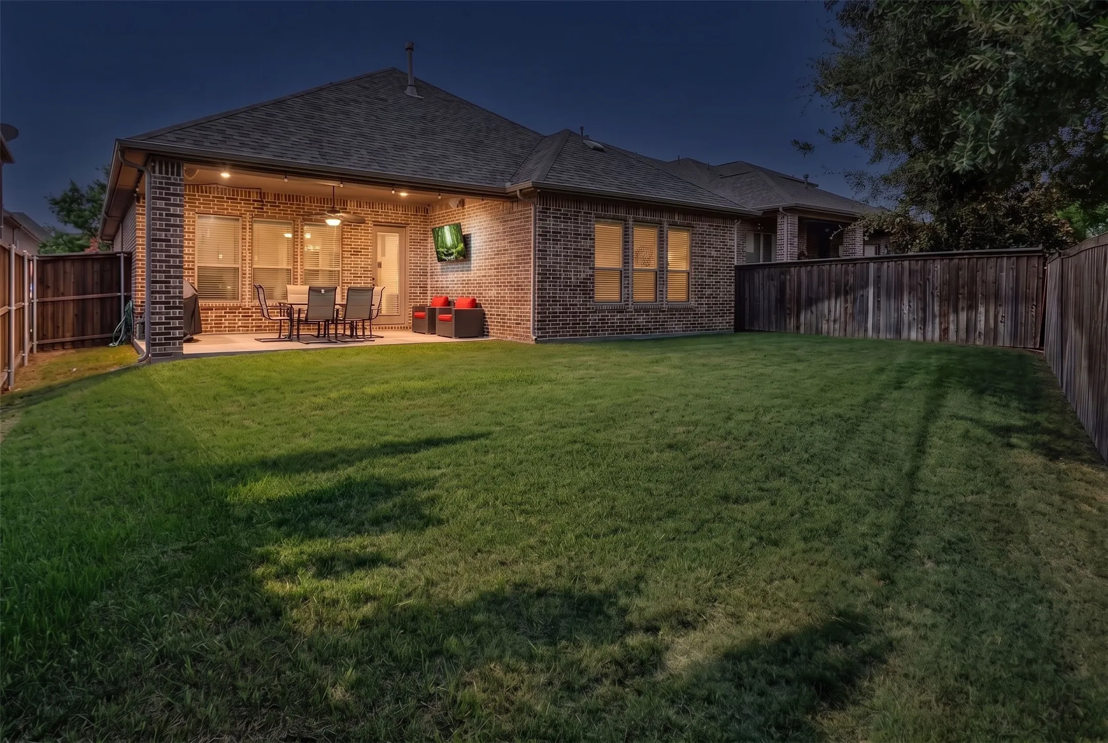Expansive backyard with a covered patio, brick exterior, and a wood privacy fence