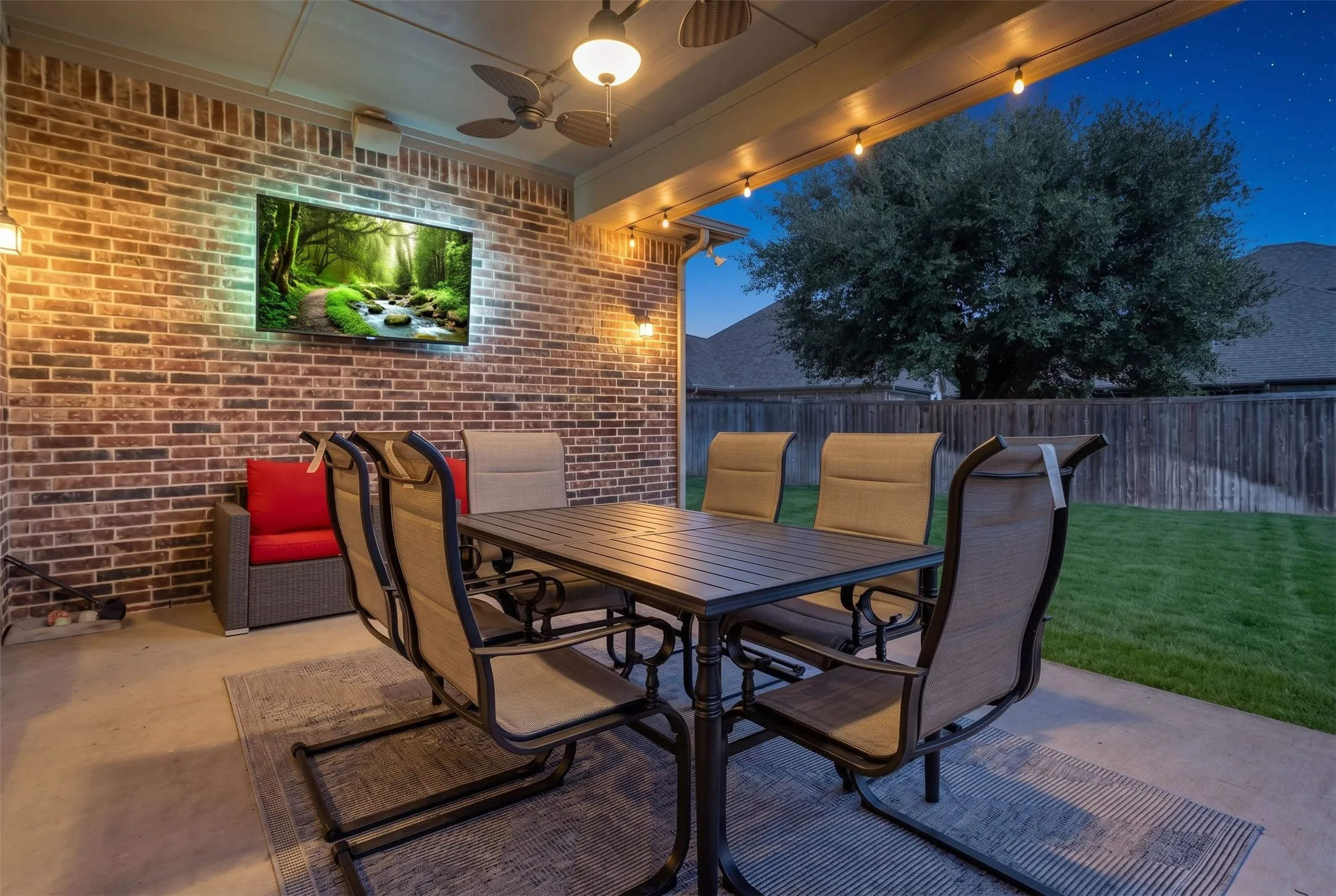 Covered patio with a ceiling fan, string lighting, and brick wall