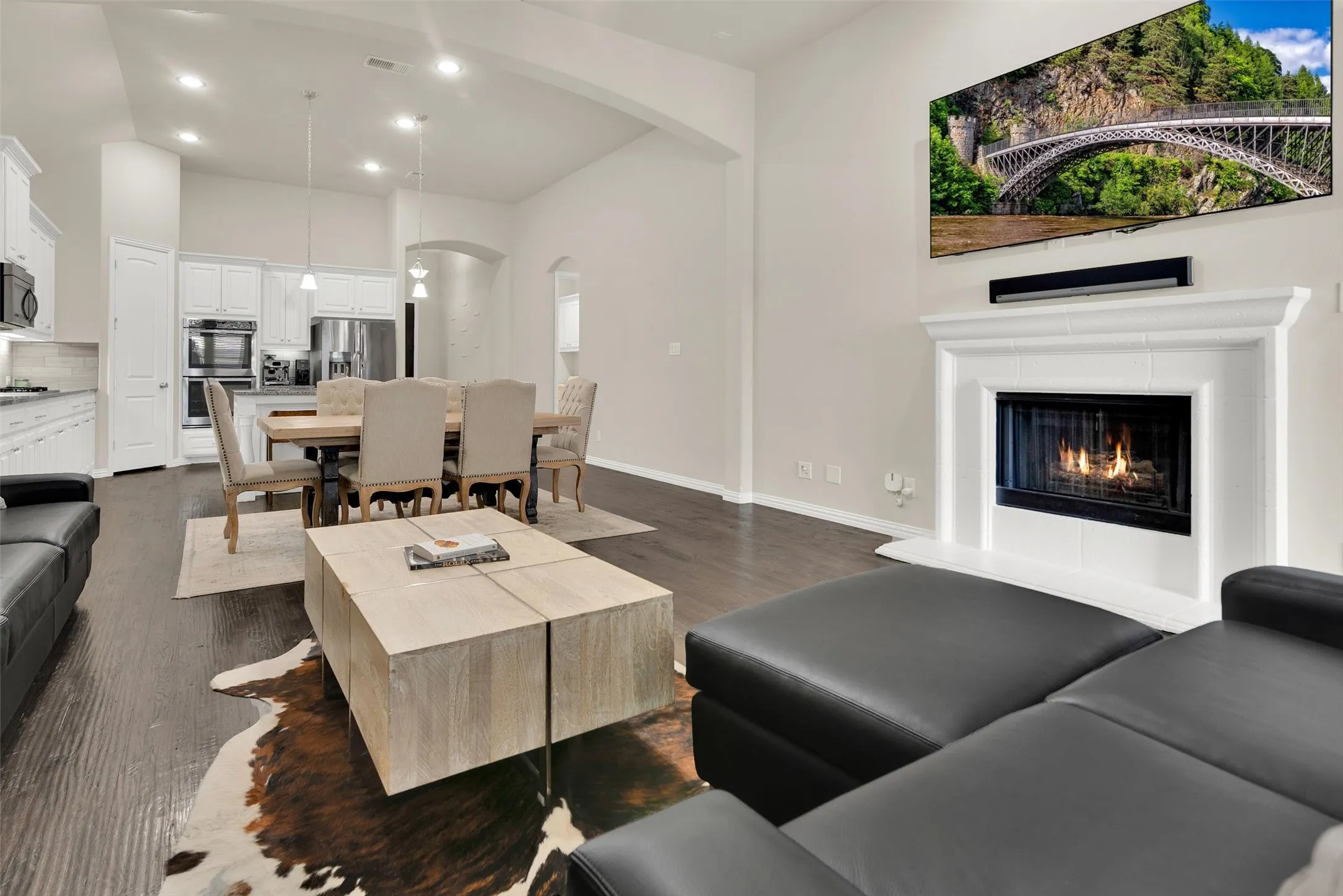 Open-concept living area featuring dark wood-finish flooring, a white mantel fireplace, vaulted ceilings, and recessed lighting