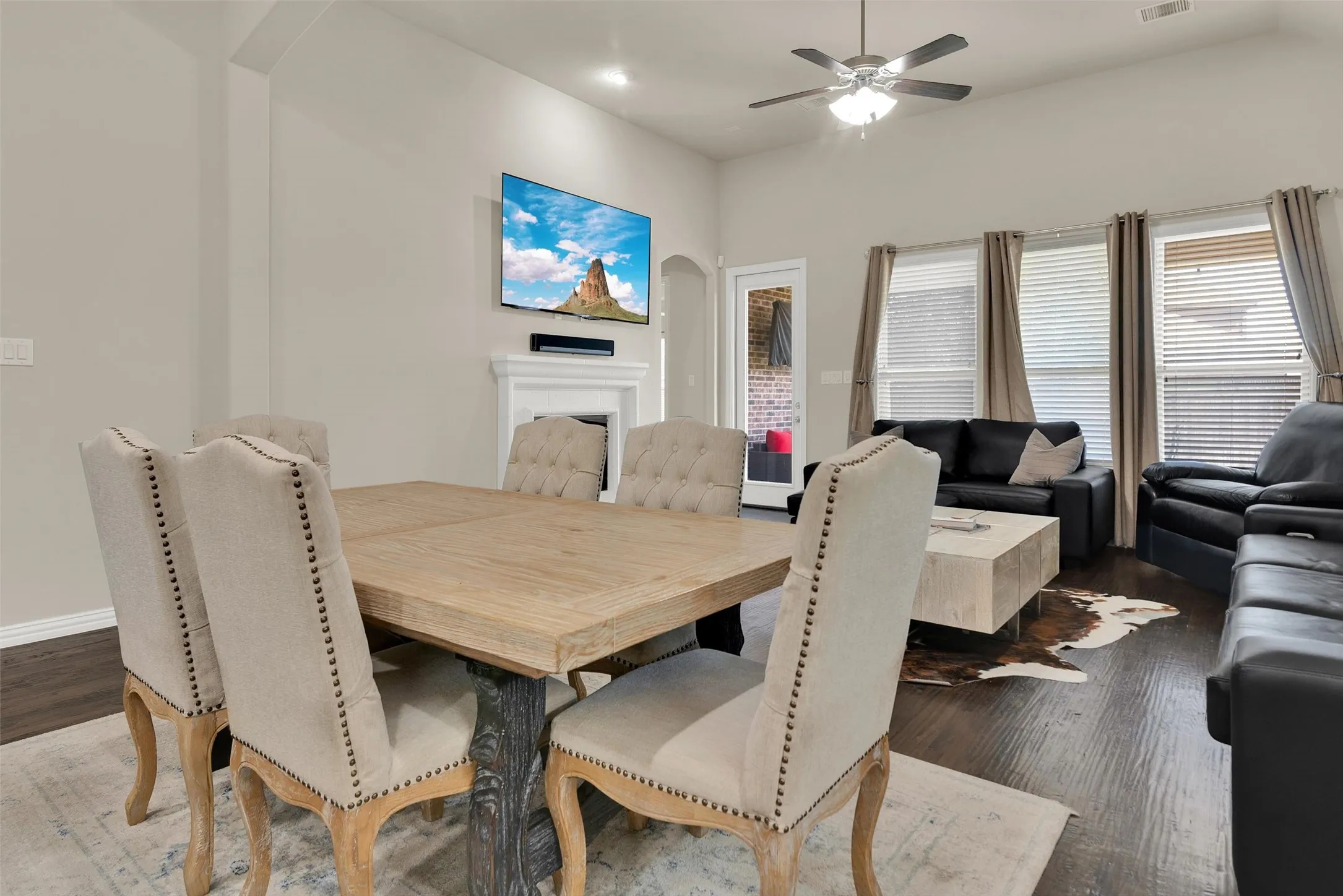 Open-concept living space with dark wood-finish flooring, a white mantel, and a ceiling fan with integrated lighting