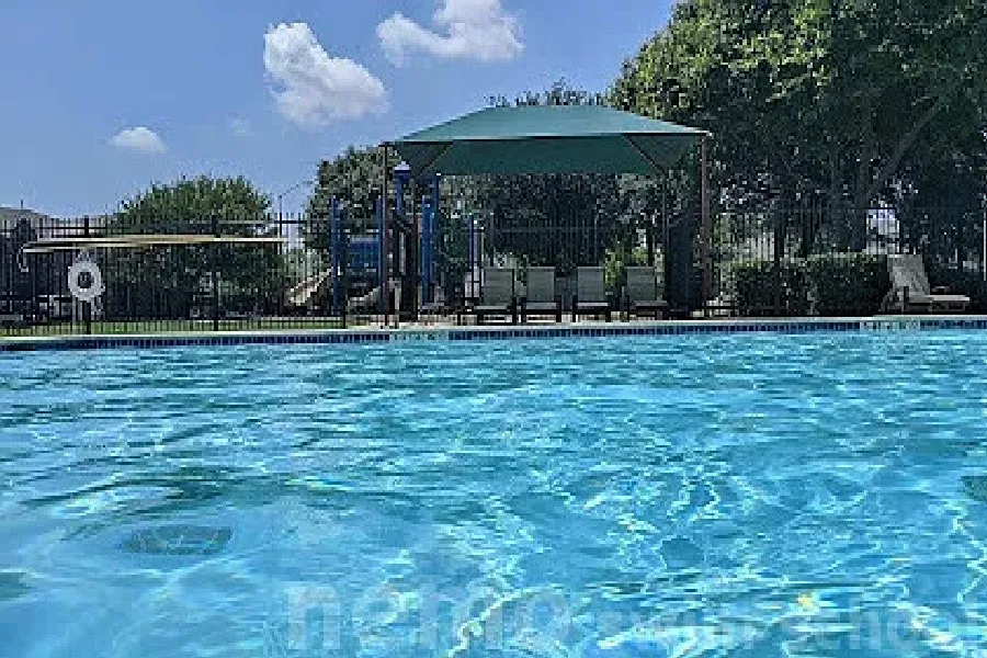 Swimming pool with a tile perimeter, a shade canopy, and a black metal fence