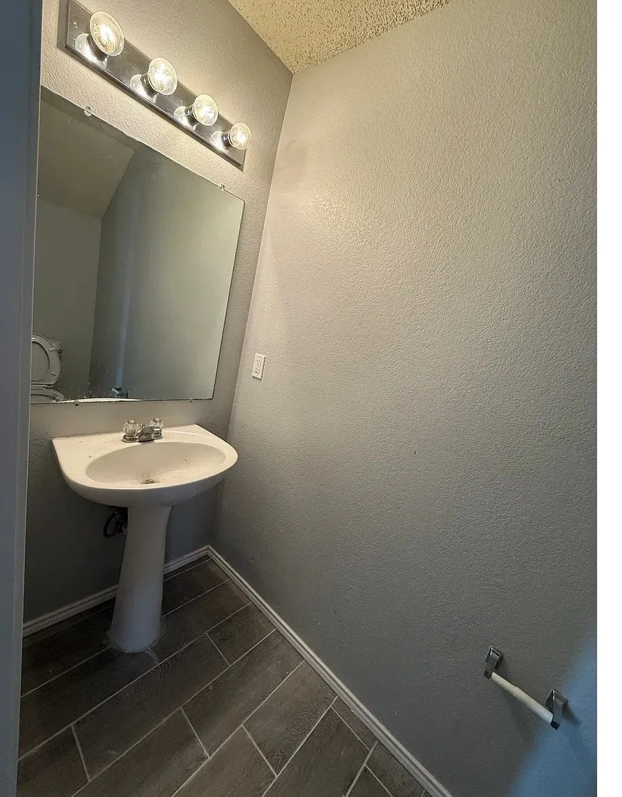Pedestal sink with chrome faucet, wall-mounted mirror, and overhead vanity lighting