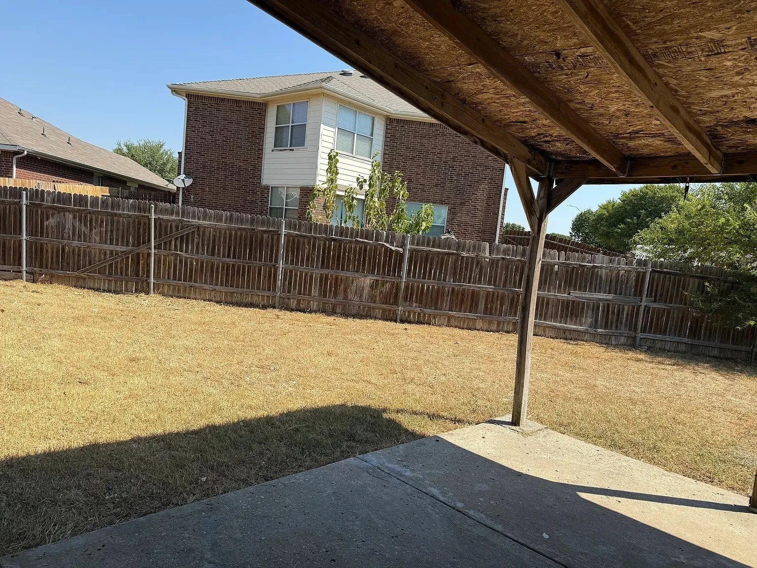 Expansive concrete patio with a covered wood-beam roof, leading to a fenced yard with a wood privacy fence