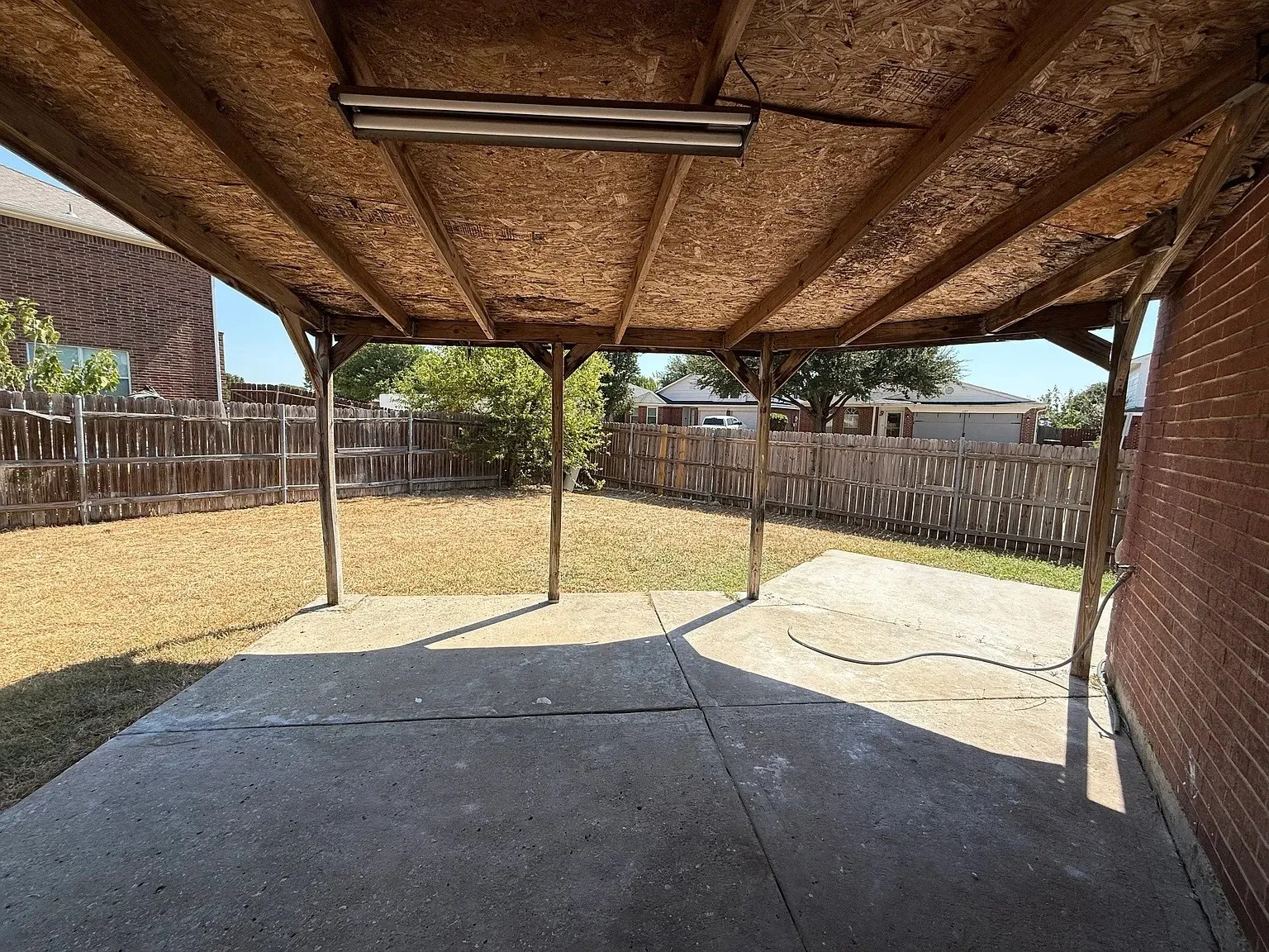 Covered patio area with concrete surfacing, exposed wooden beam ceiling, and brick exterior wall