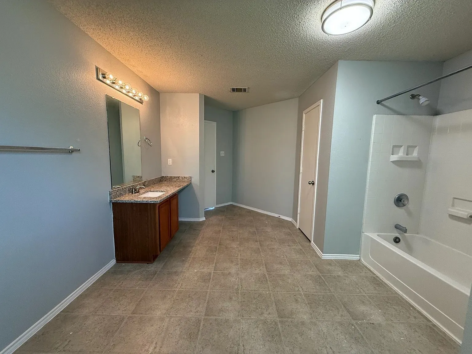 Dual sink vanity with stone countertop, tile flooring, and integrated bathtub with shower