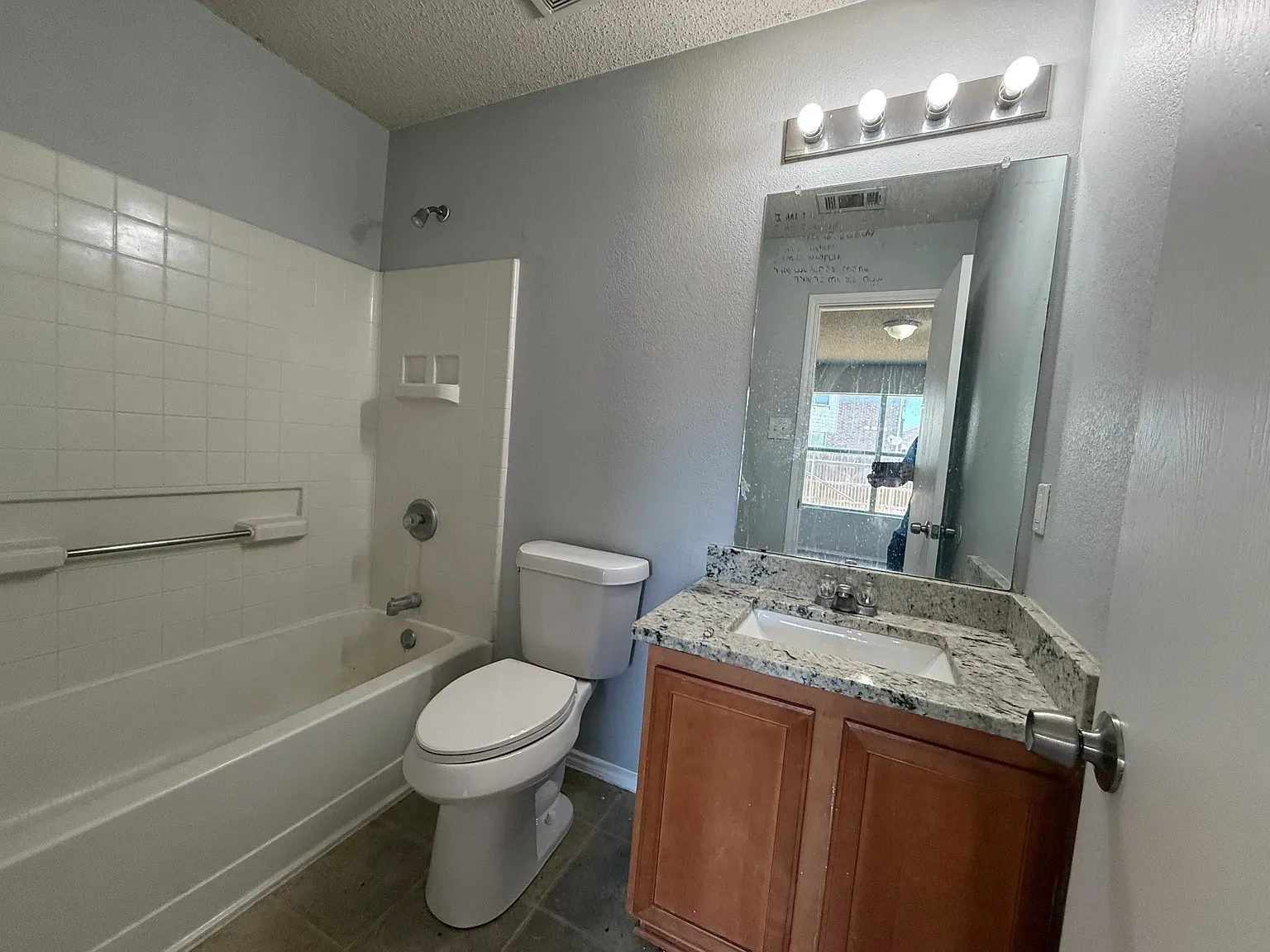 Bathroom featuring a white tub, white tiled surround, toilet, and a vanity with a countertop and under-mount sink