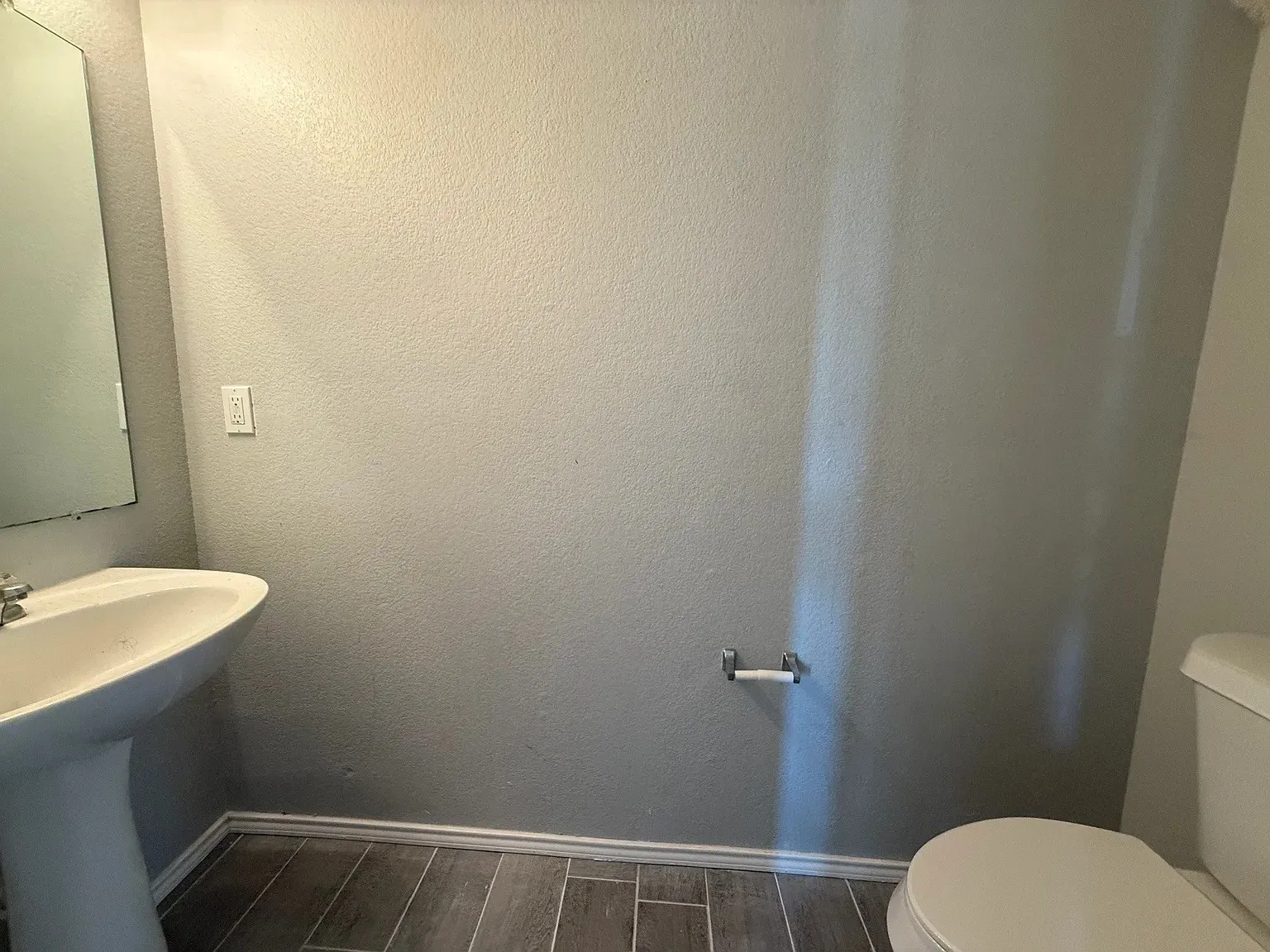 Pedestal sink with chrome faucet, light gray painted walls, and wood-finish tile flooring