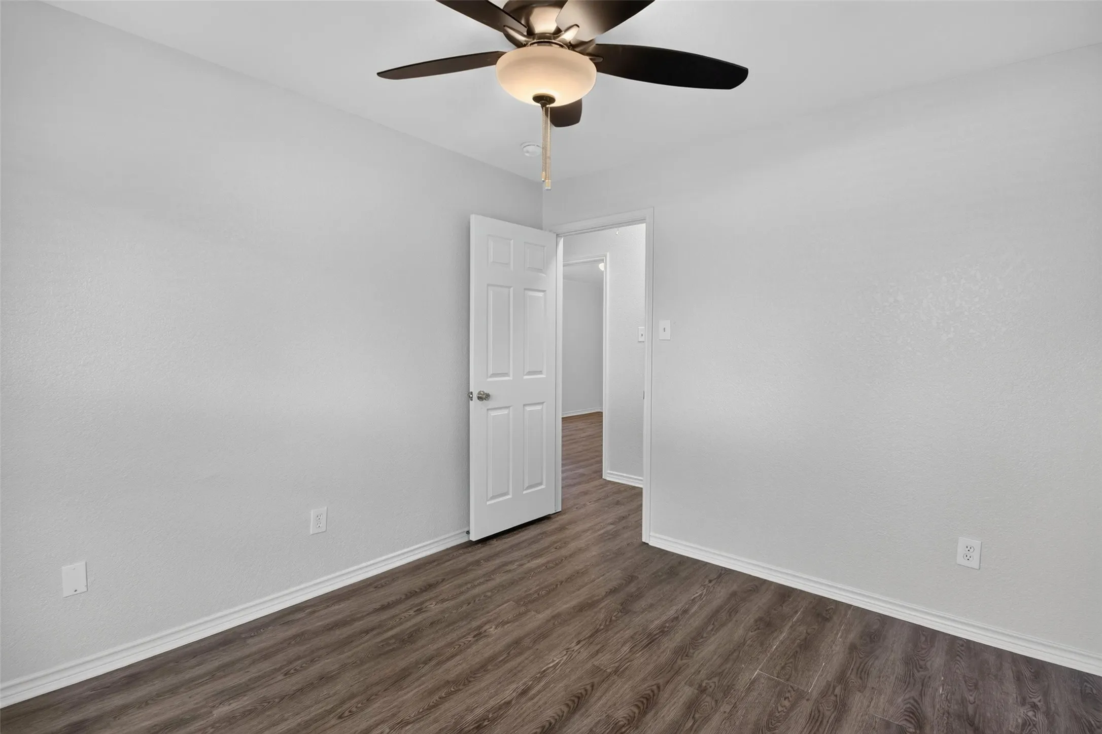 Wood-finish flooring, ceiling fan with integrated lighting, paneled interior door, and light-toned wall finishes