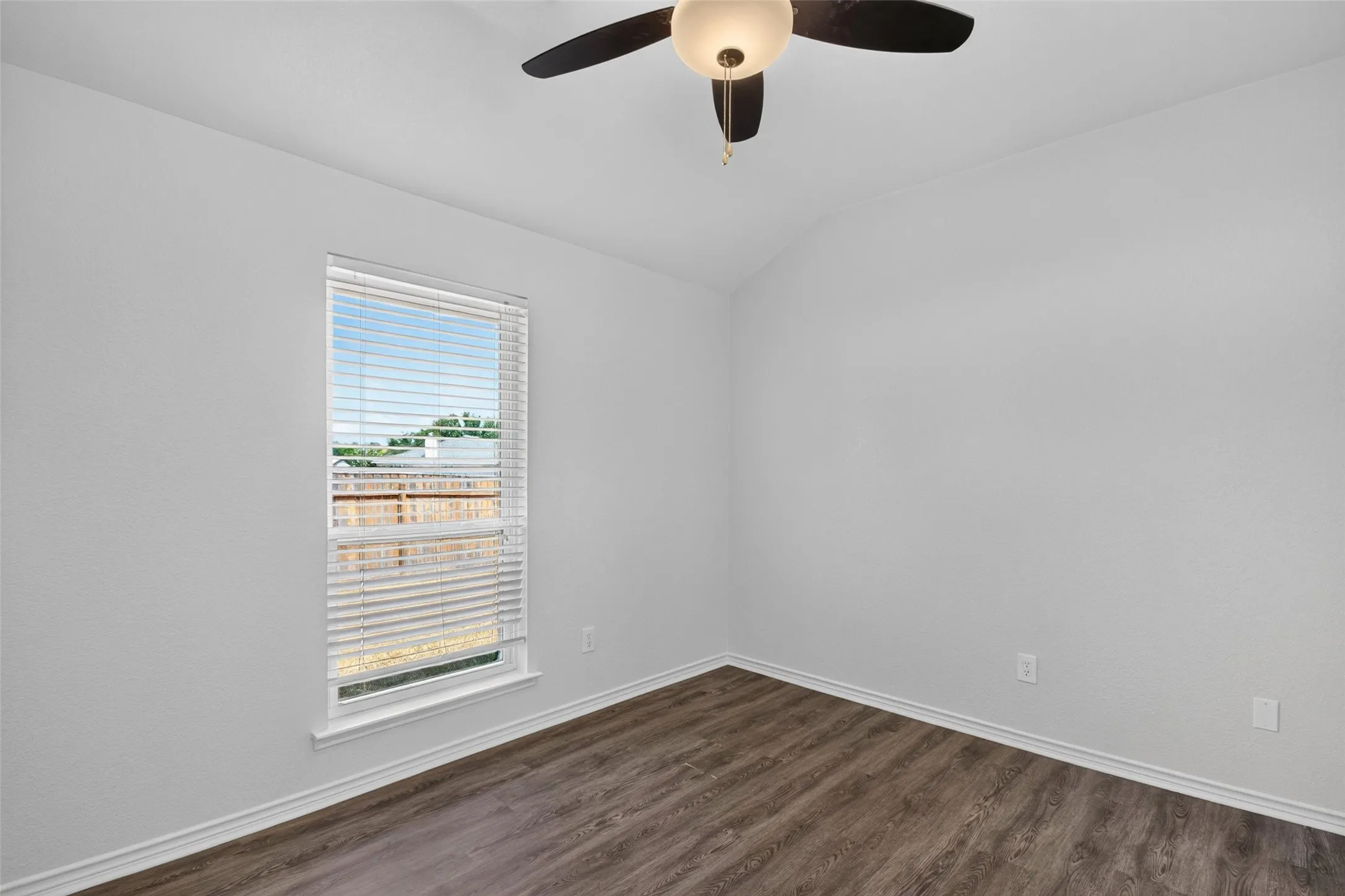 Vaulted ceiling with a ceiling fan light fixture, wood-finish flooring, and a window with blinds