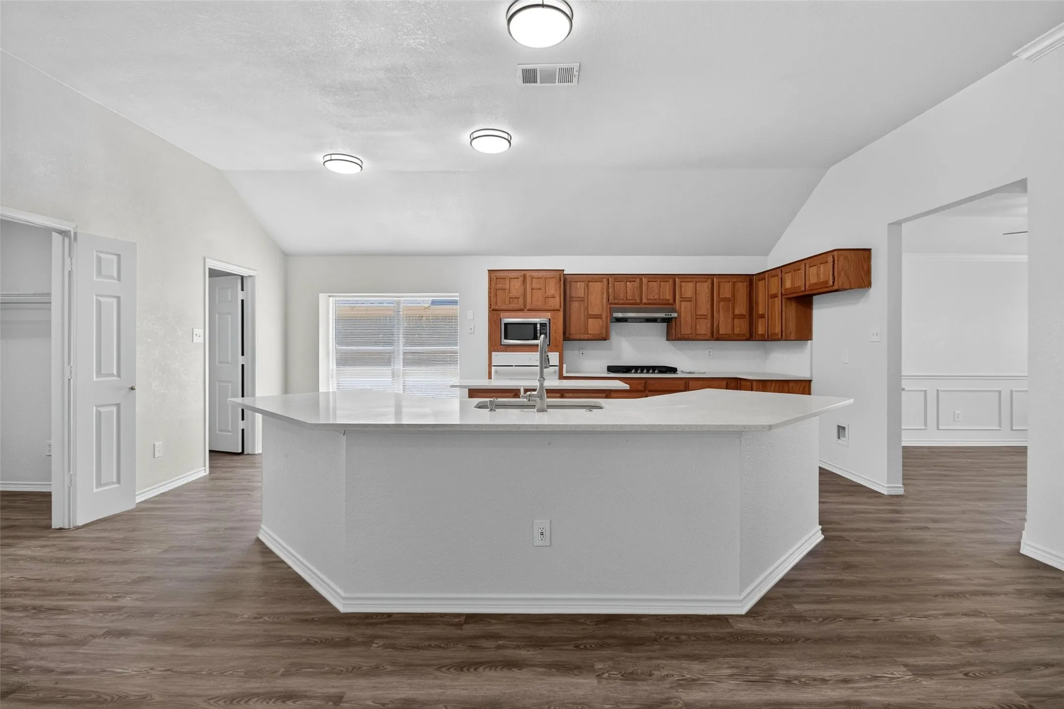 Kitchen featuring an island with a light-toned countertop, wood-finish cabinetry, stainless steel appliances, and wood-finish flooring