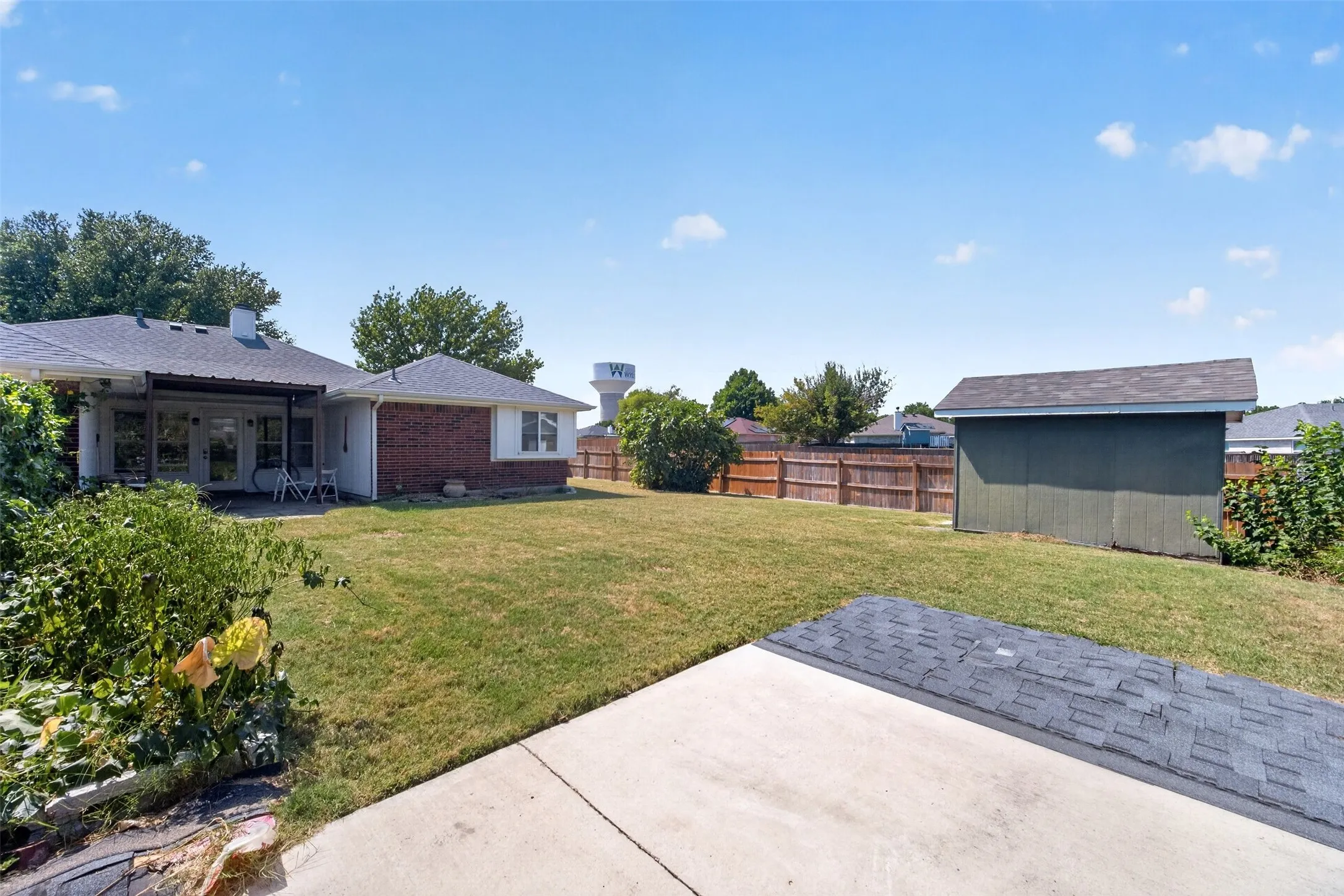 Expansive rear yard featuring green lawn, a privacy fence, and a detached storage shed
