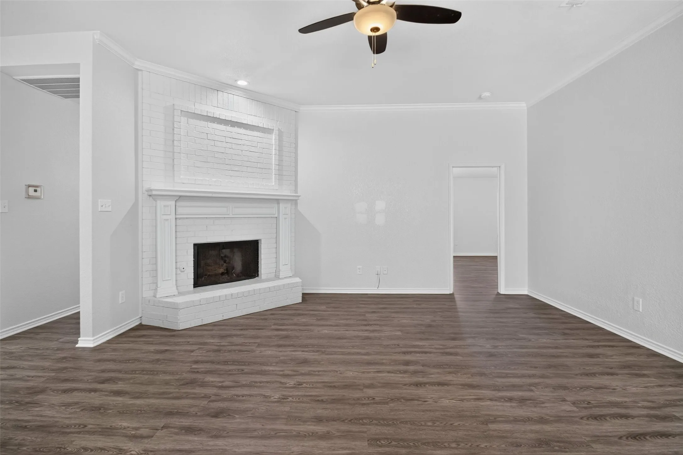 Spacious living room featuring wood-finish flooring, a fireplace with white subway tile surround, ceiling fan with brass accents, and abundant natural light from dual windows with plantation shutters