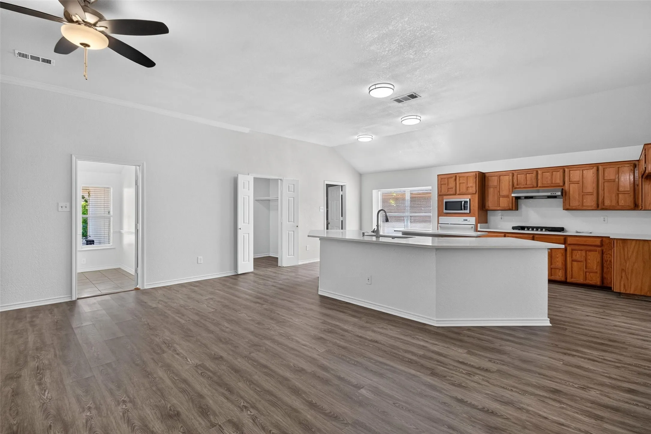 Open-concept living space featuring wood-finish flooring, vaulted ceilings, and a ceiling fan with integrated lighting