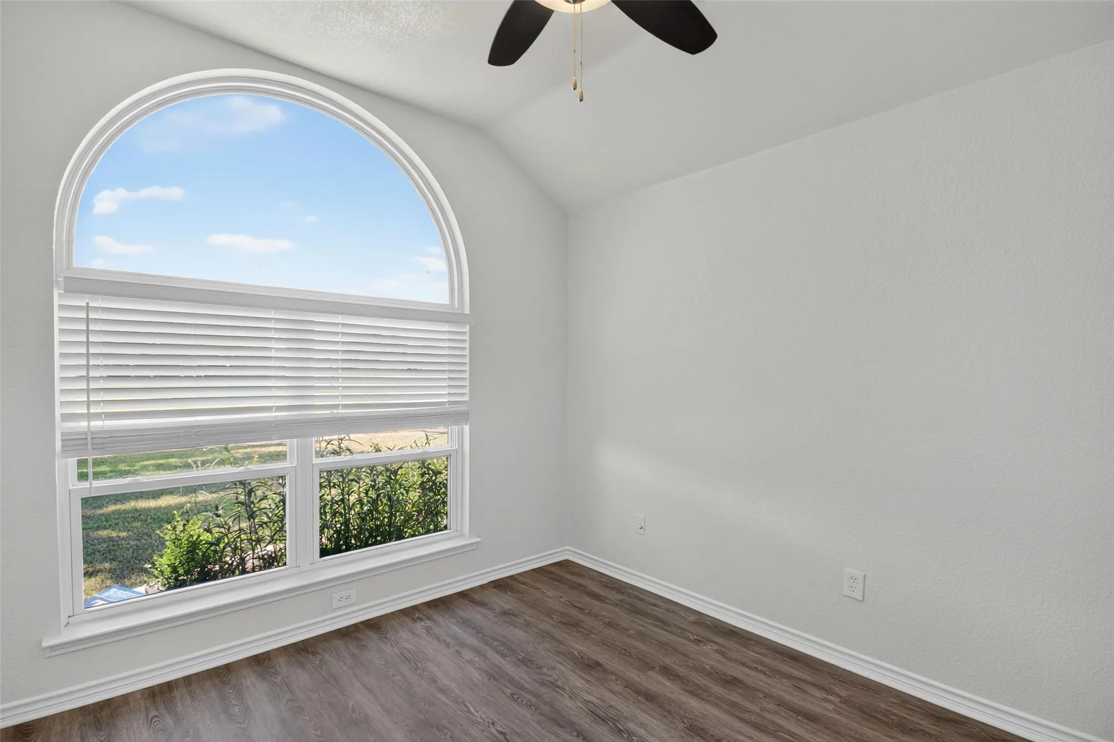 Arched window with integrated blinds, wood-finish flooring, vaulted ceiling, and ceiling fan