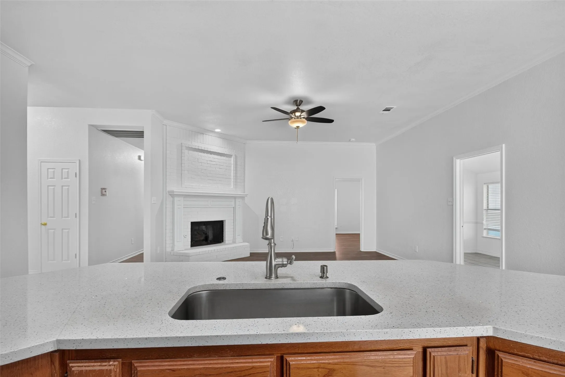 Kitchen island with a built-in sink and stainless steel faucet, wood cabinetry, painted brick fireplace, and a ceiling fan with integrated lighting
