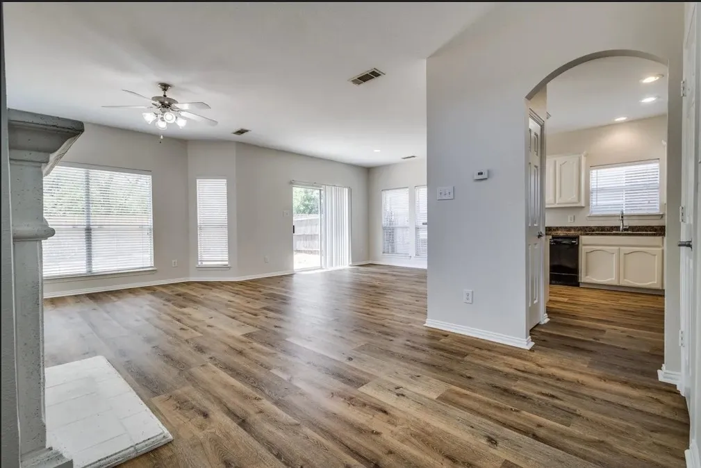 Expansive living area featuring wood-finish flooring, a ceiling fan, and multiple windows with blinds