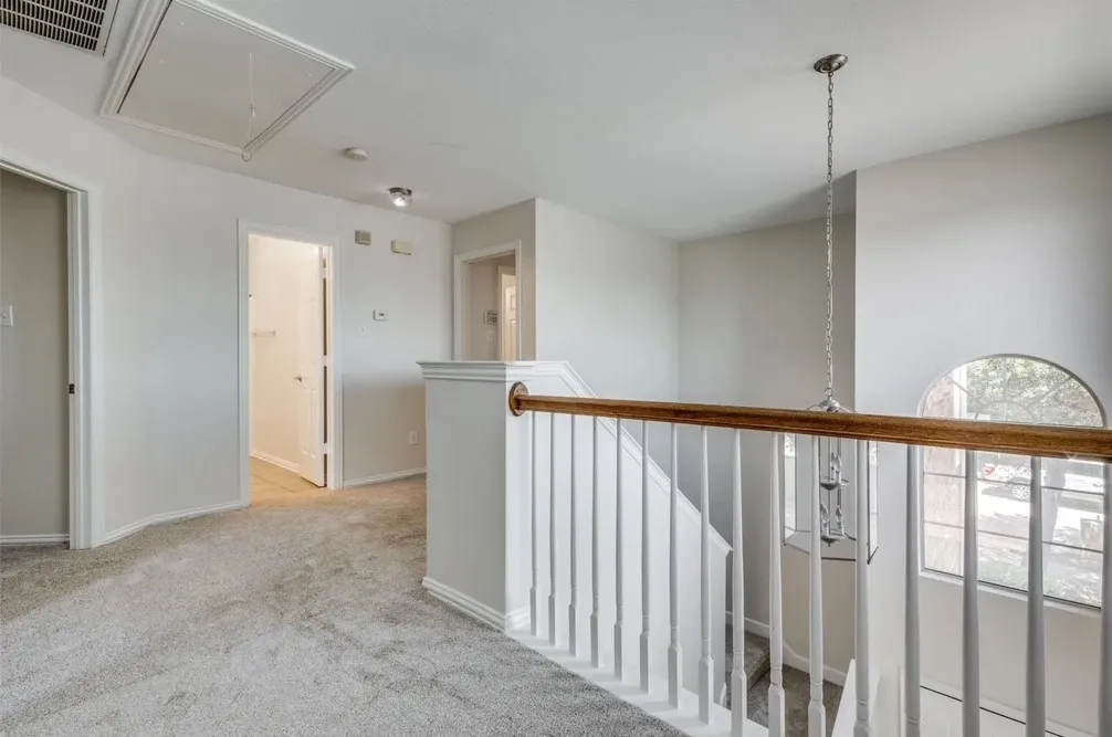 Carpeted hallway with white walls, white wood-finish railing, and an arched window