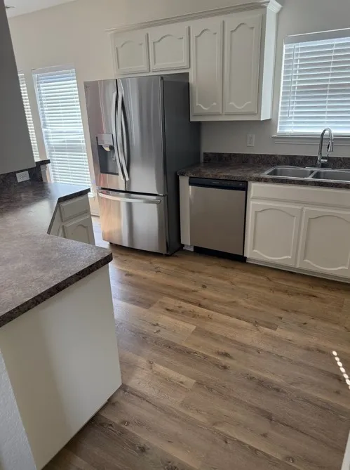 Kitchen featuring wood-finish flooring, white cabinetry, stainless steel appliances, and a dual basin sink