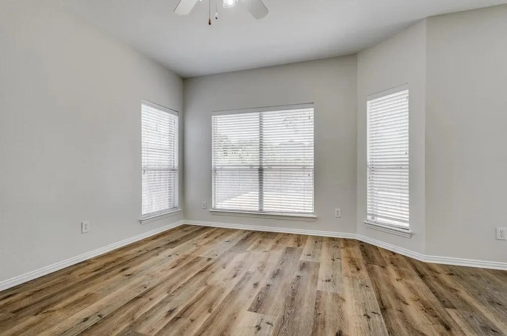 Vaulted ceiling with a ceiling fan, multiple windows with blinds, and wood-finish flooring